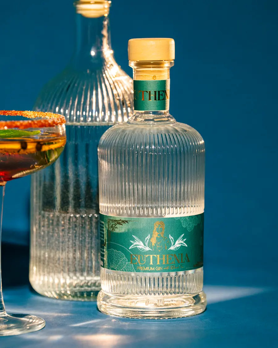Bouteille de Gin Euthénia, coupe de cocktail et flacon dégustation sur fond bleu