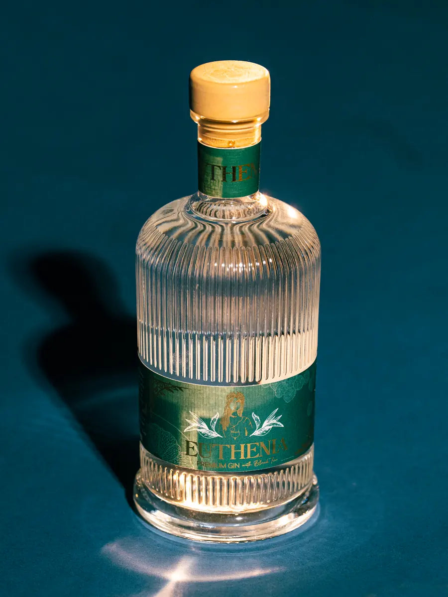 Bouteille de Gin Euthénia debout sous un projecteur, sur fond bleu